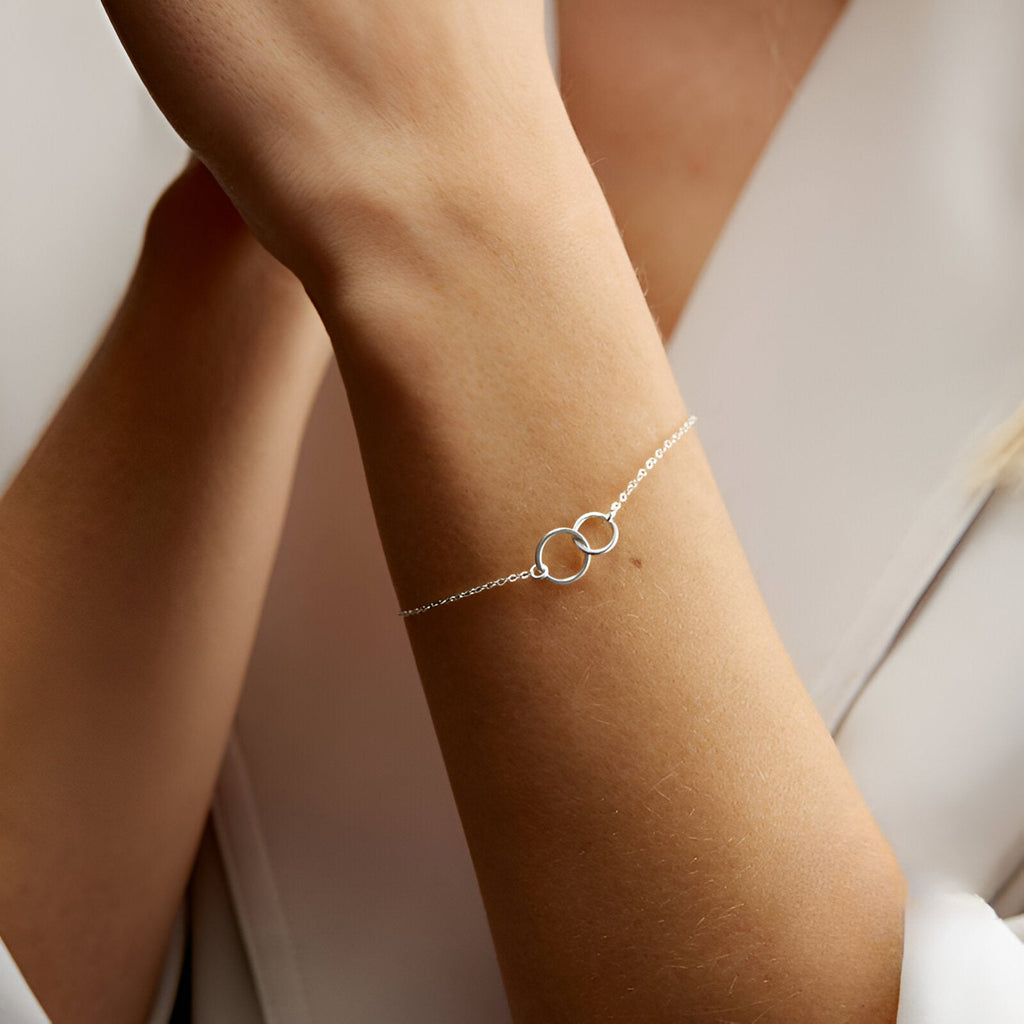 Bracelet fin en argent sterling avec deux cercles entrelacés sur poignet féminin.