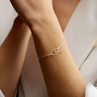 Bracelet fin en argent sterling avec deux cercles entrelacés sur poignet féminin.
