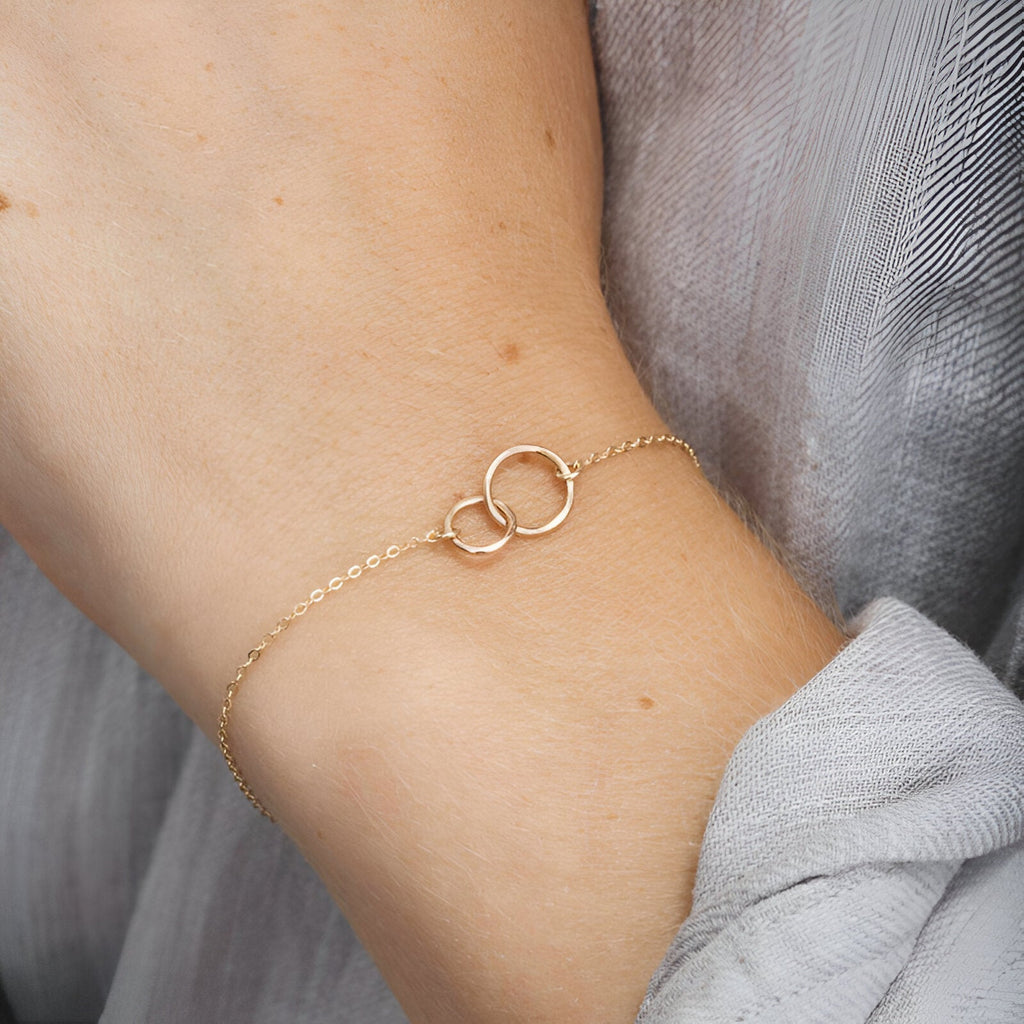 Bracelet fin en argent sterling avec deux cercles entrelacés porté au poignet féminin.