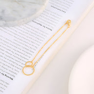 Bracelet en or avec duo de cercles entrelacés suspendus à une chaîne fine délicate.
