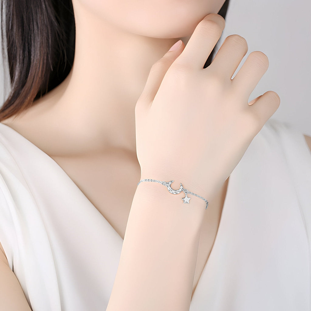 Bracelet fin en argent sterling avec pendentifs étoile et lune délicats porté au poignet féminin.