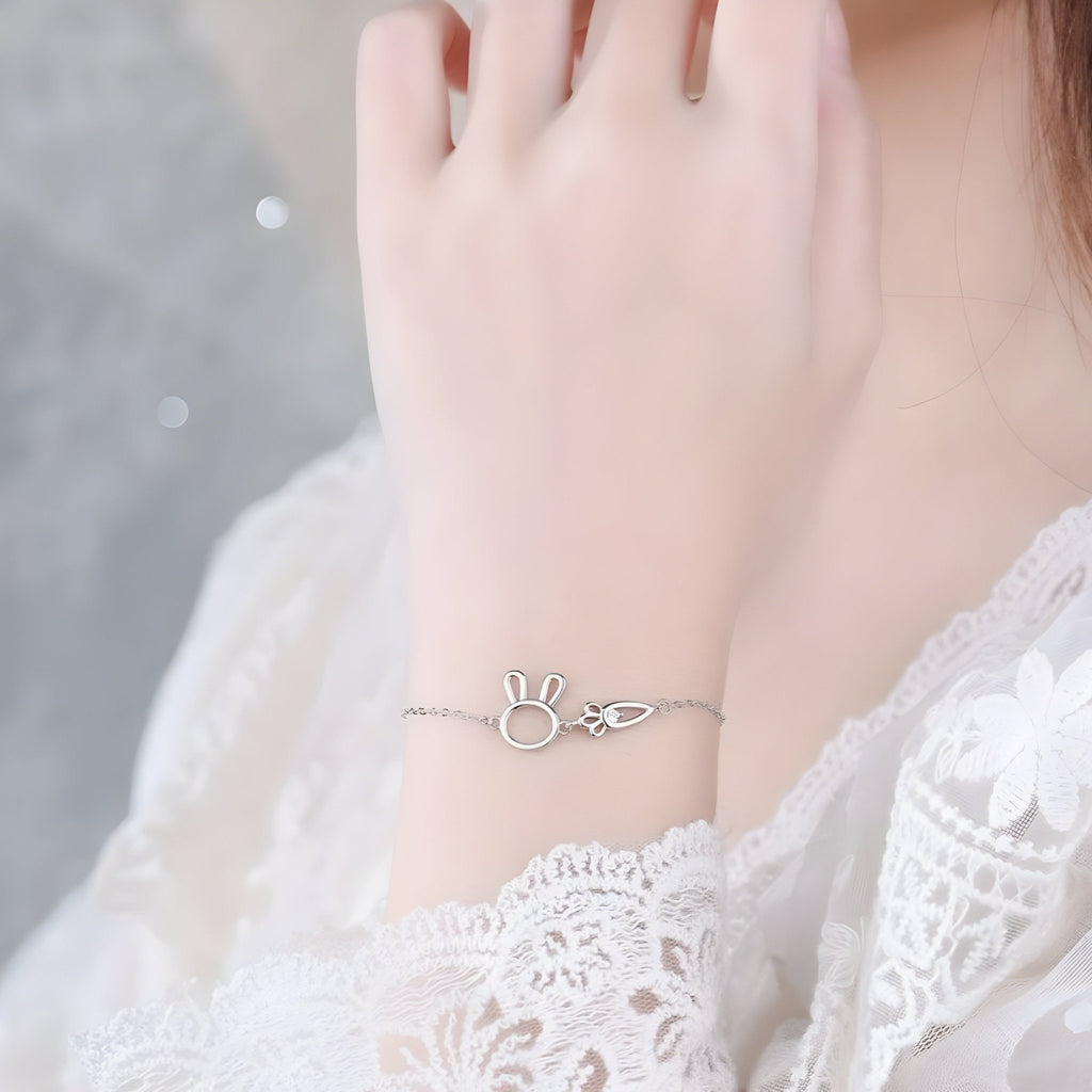 Bracelet fin en argent sterling avec pendentifs lapin et carotte délicats sur poignet féminin.