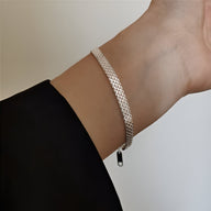 Bracelet tressé en argent sterling délicat porté au poignet féminin, finition brillante.