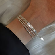 Bracelet tressé en argent sterling à trois rangs avec plaquette fine, porté au poignet féminin.