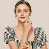 Bracelet en argent sterling avec motif de feuille scintillante porté par femme au teint clair en robe à carreaux noir et.