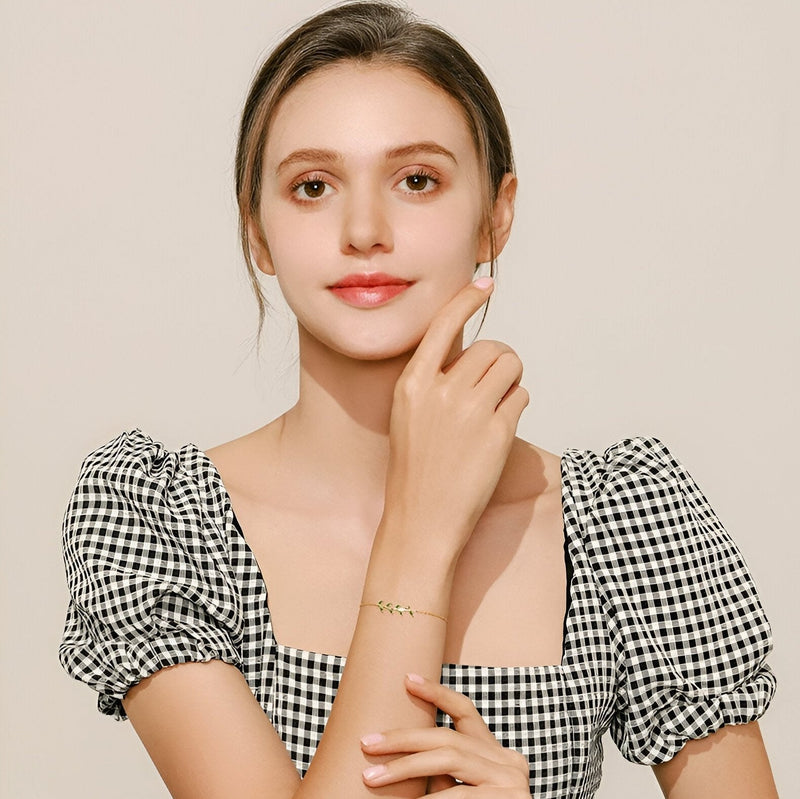 Bracelet en argent sterling avec motif de feuille scintillante porté par femme au teint clair en robe à carreaux noir et.