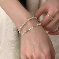 Bracelet fin en argent sterling avec petit noeud ruban délicat porté au poignet.