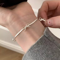 Bracelet en argent sterling fin avec petit noeud ruban délicat, porté au poignet féminin.