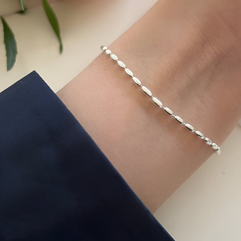 Bracelet fin en argent sterling avec maillons style grain de riz sur poignet féminin.