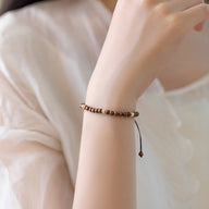 Bracelet fin en bois de santal marron avec perles rondes, ajustable par nœud coulissant, porté au poignet féminin.