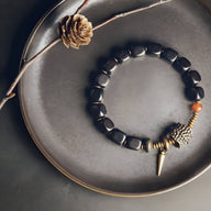 Bracelet en bois d'ébène noir avec perles antique en cuivre et pendentif cône sur assiette grise.