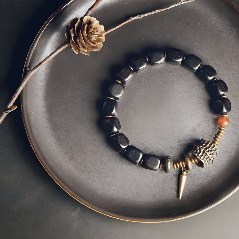 Bracelet en bois d'ébène noir avec perles antique en cuivre et pendentif cône sur assiette grise.