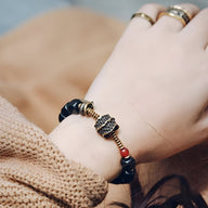 Bracelet en bois d'ébène noir avec détails cuivrés antiques et perle rouge, porté au poignet féminin.