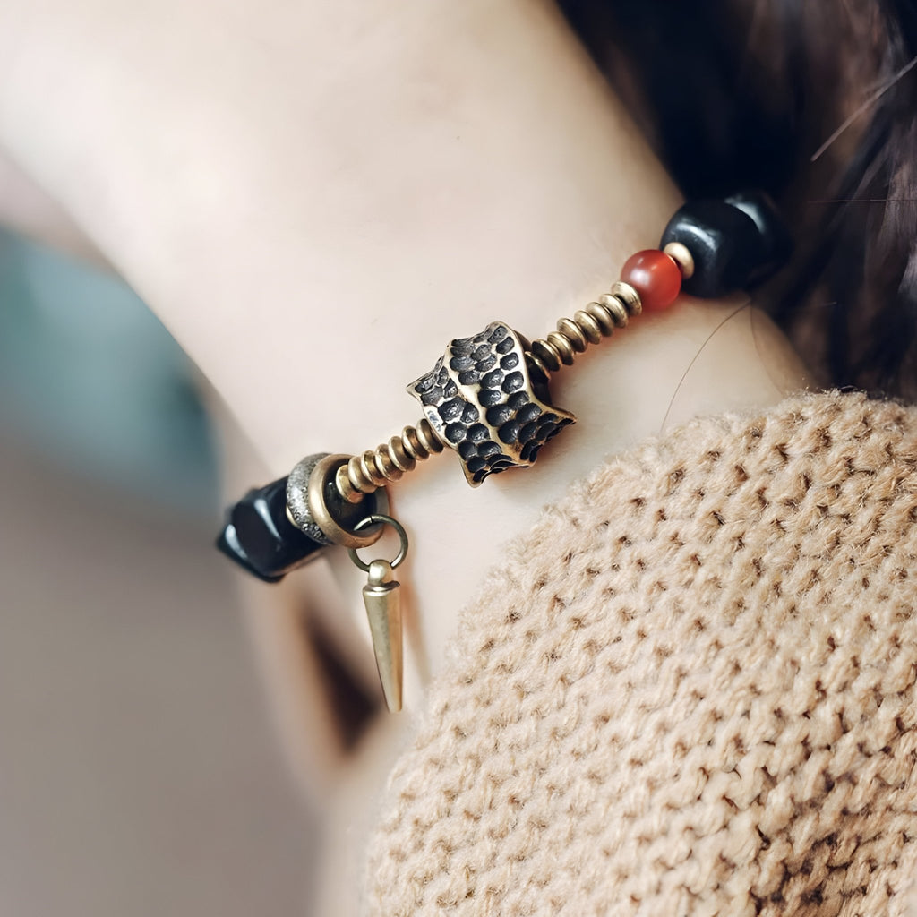Bracelet en bois d'ébène noir avec détail antique en métal doré et pendentif cône, porté au poignet féminin.