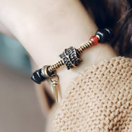 Bracelet en bois d'ébène noir avec détail antique en métal doré et pendentif cône, porté au poignet féminin.