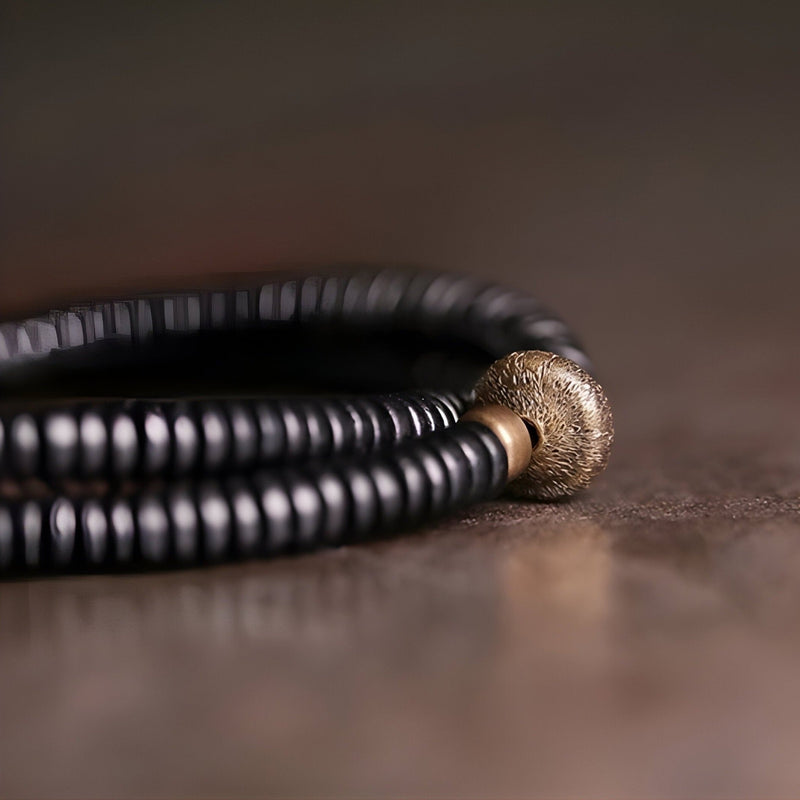 Bracelet fin en perles de bois d'ébène noir avec un détail en cuivre texturé.
