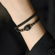 Bracelet double en bois d'ébène noir avec perles cuivrées et motif central sculpté.