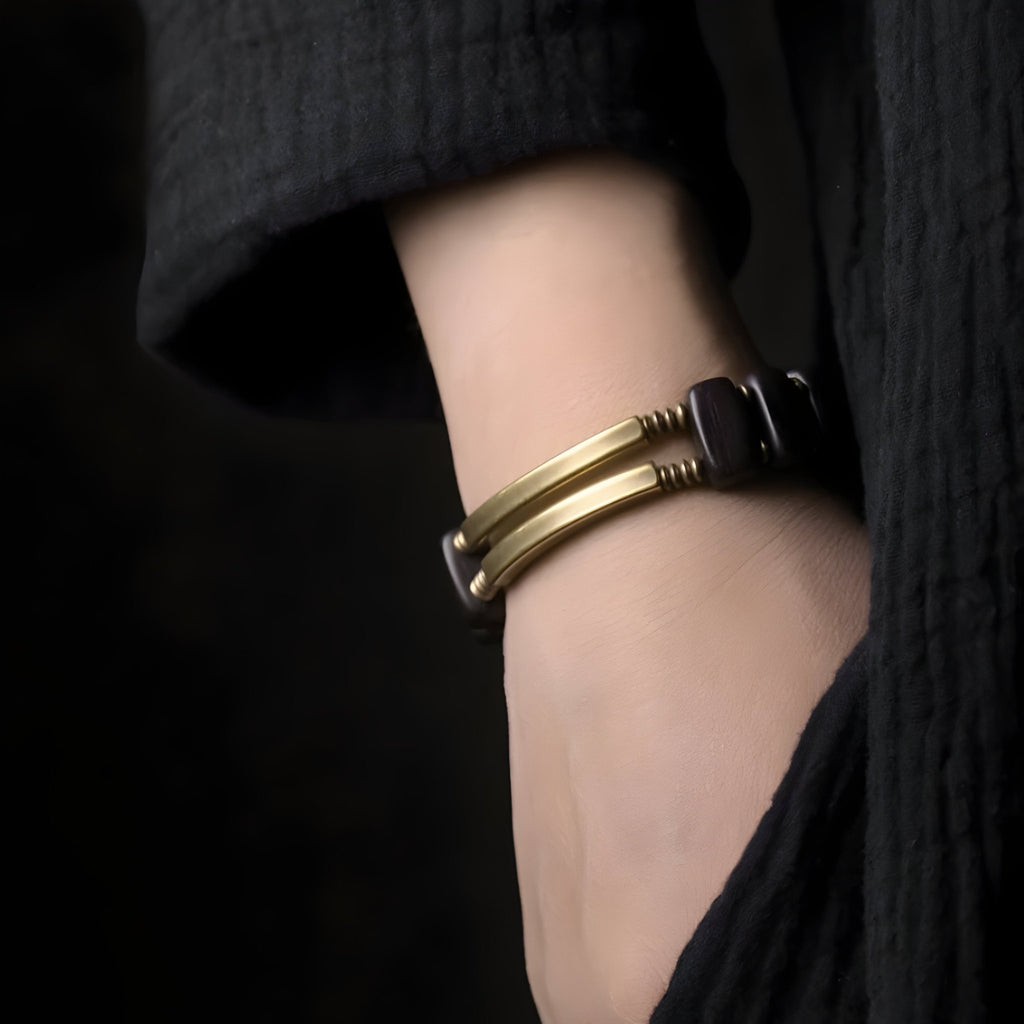 Bracelet flexible en bois d'ébène noir avec détails en cuivre, porté au poignet féminin.