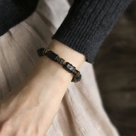 Bracelet mixte en bois d'ébène noir avec éléments en laiton sur poignet, style naturel et élégant.