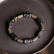 Bracelet mixte en bois d’ébène noir sculpté et éléments en laiton doré sur fil élastique.