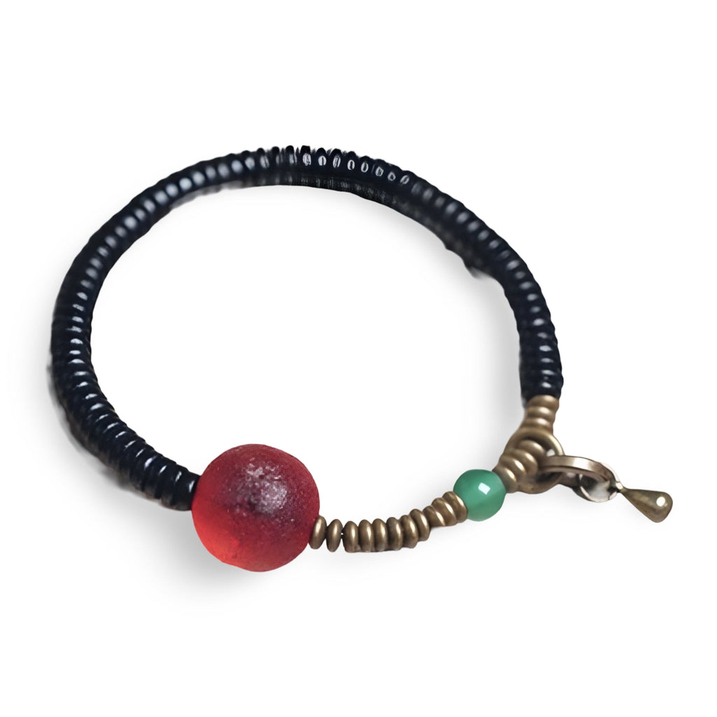 Bracelet fin en bois d'ébène noir avec perle en verre rouge translucide et petite perle verte près du fermoir en métal doré.