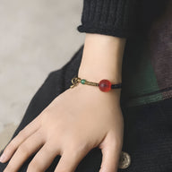 Bracelet fin en bois d’ébène noir avec perle rouge translucide et cordon ajustable.