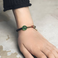 Bracelet en bois d'ébène noir avec perle verte en verre et fermoir doré, style minimaliste pour femme.