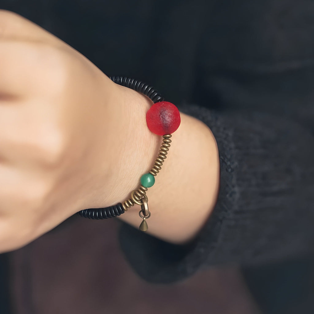 Bracelet fin en bois d'ébène noir avec perle rouge translucide et détail en métal bronze.