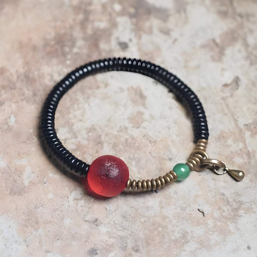 Bracelet en bois d’ébène noir avec perle en verre rouge et détail vert, fermoir en métal doré.