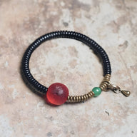 Bracelet en bois d’ébène noir avec perle en verre rouge et détail vert, fermoir en métal doré.