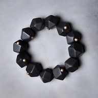 Bracelet femme en bois d’ébène noir à perles géométriques hexagonales avec petits détails métalliques dorés.