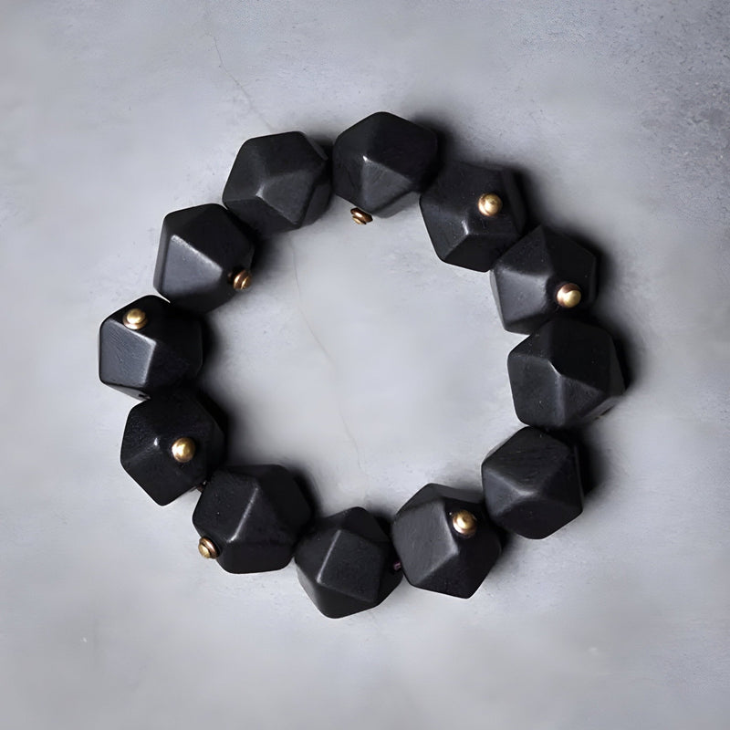 Bracelet femme en bois d’ébène noir à perles géométriques hexagonales avec petits détails métalliques dorés.