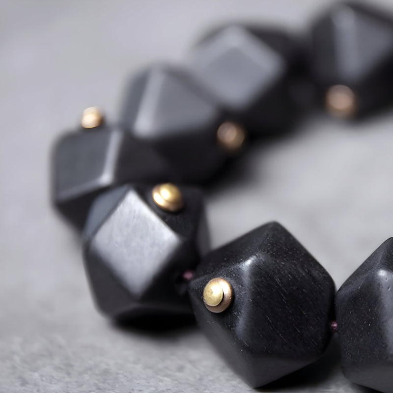 Bracelet femme en bois d’ébène noir mat avec perles dorées, style géométrique moderne.