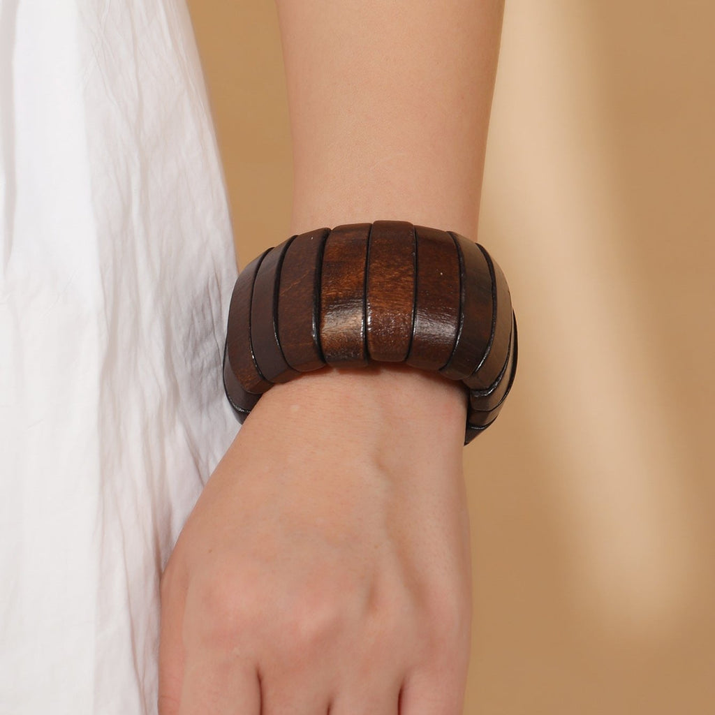 Bracelet large en bois naturel de teinte café avec segments lisses, porté au poignet féminin.