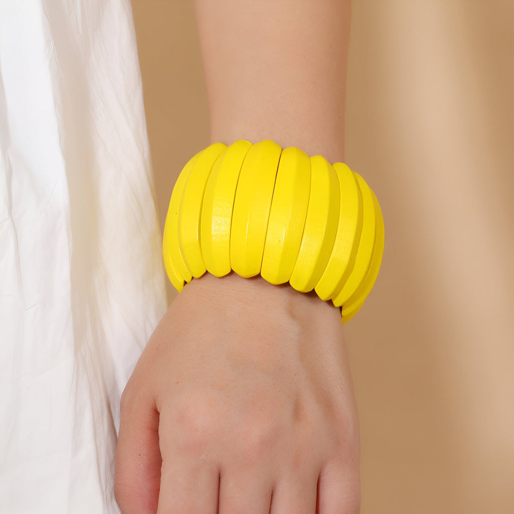 Bracelet large en bois naturel peint en jaune vif, style ethnique, porté au poignet féminin.