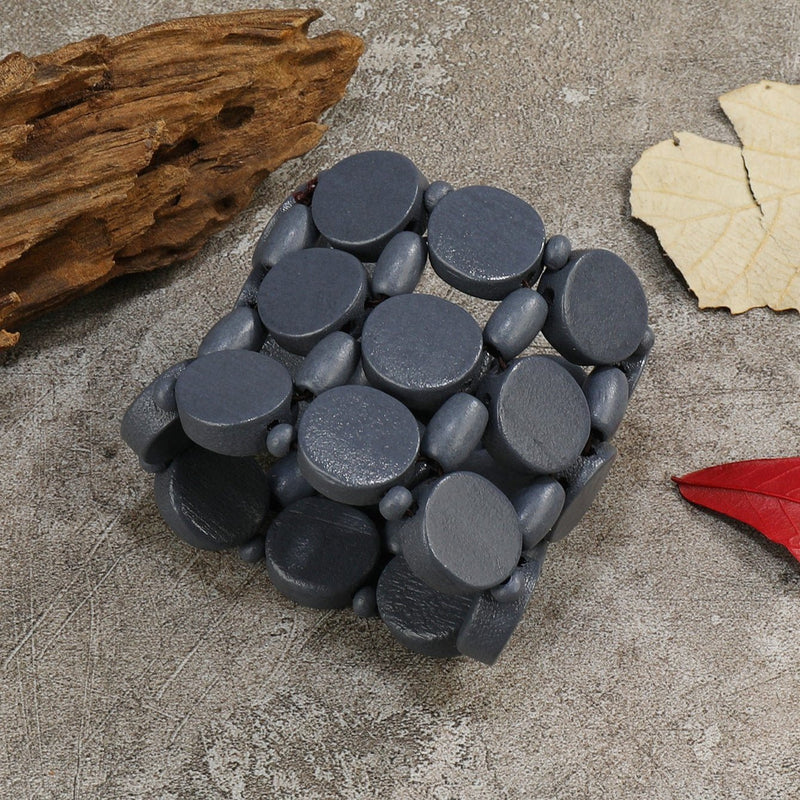 Bracelet large en bois naturel peint noir avec éléments ovales et ronds assemblés.