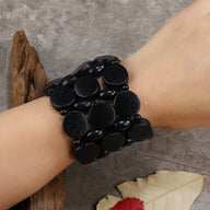 Bracelet large en bois noir composé de disques lisses et ovales, style original pour femme.