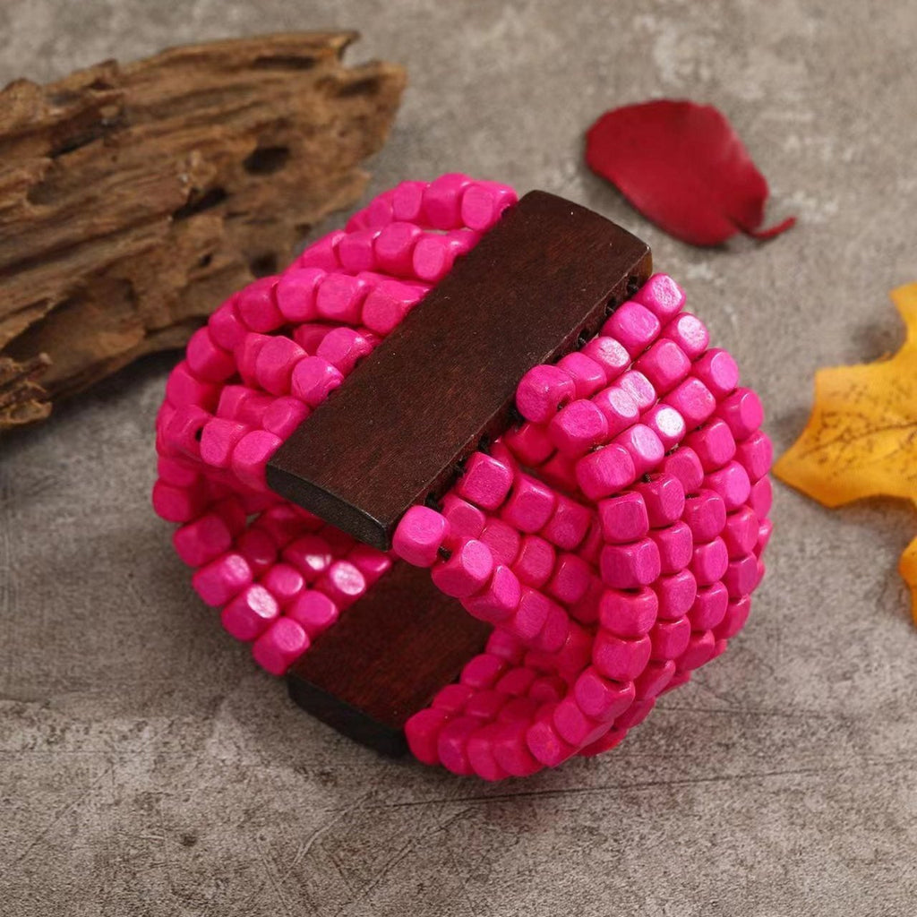 Bracelet en bois naturel avec perles roses vives tissées et fermoir en bois foncé aux bords arrondis.