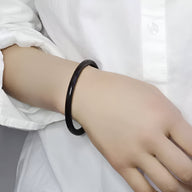 Jonc bracelet fin en bois noir naturel, finition lisse et brillante, porté au poignet féminin.