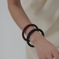 Bracelets joncs élégants en bois naturel marron et noir portés au poignet féminin sur fond neutre.