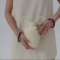 Bracelet jonc en bois naturel marron et noir porté sur les poignets d'une femme en robe crème avec vase blanc moderne.