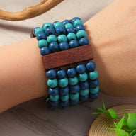 Bracelet manchette en perles de bois bleu turquoise et bleu foncé avec barre en bois brun sur poignet féminin.