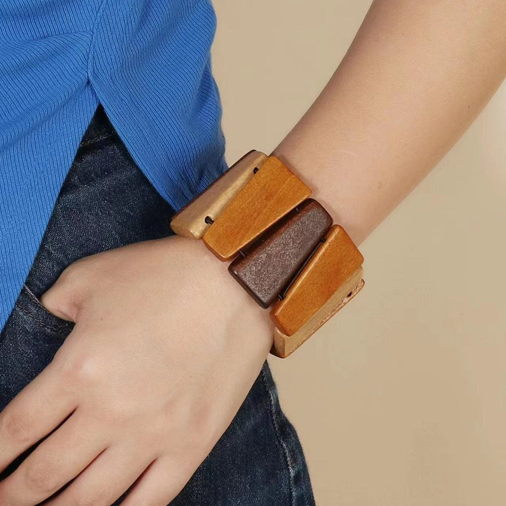 Bracelet manchette en bois naturel marron aux formes géométriques porté au poignet féminin.