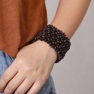 Bracelet large en bois naturel couleur café avec motif floral en relief, porté au poignet féminin.