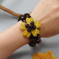 Bracelet en coquille de noix de coco brun foncé avec fleur des îles jaune orné de perles brunes.