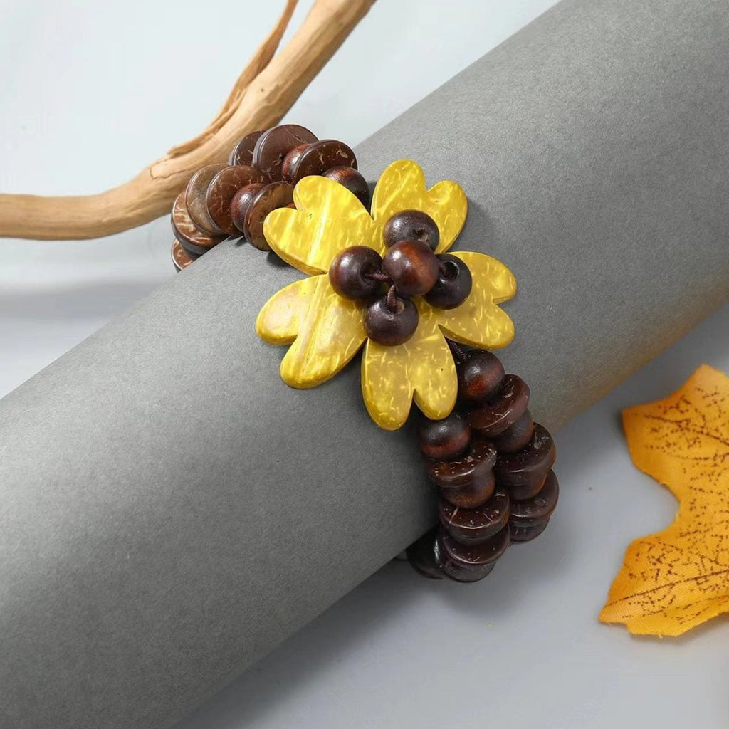 Bracelet triple rang en coquilles de noix de coco marron avec fleur jaune des îles au centre.