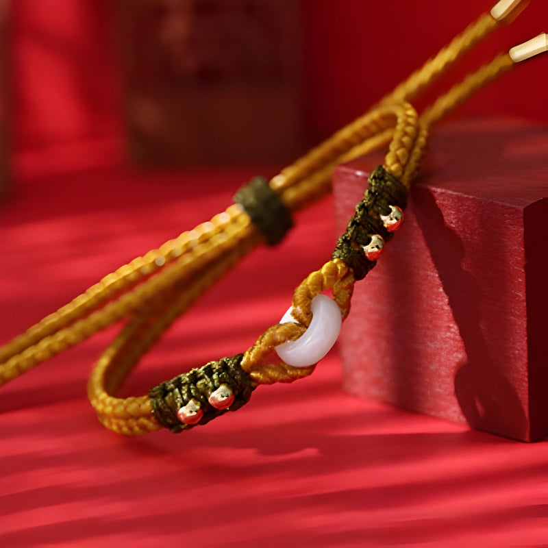 Bracelet en corde tressée jaune avec pierre de jade blanche et fermoir en métal noir orné d’éclats dorés.