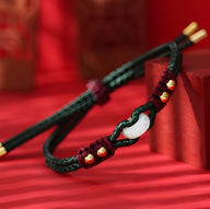 Bracelet en corde tressée noire et rouge avec pierre de jade blanche et petits accents dorés.