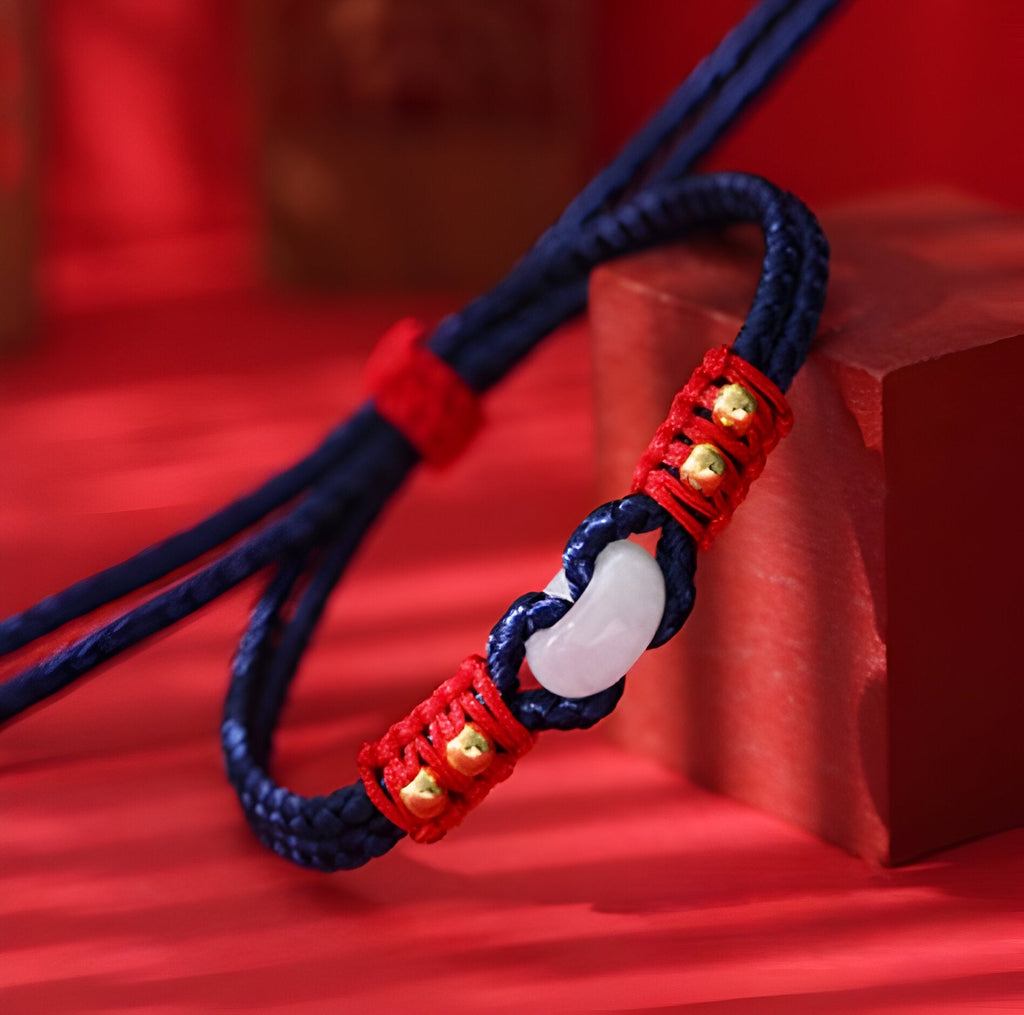 Bracelet en corde bleue tressée avec pierre de jade blanche et détails rouges et dorés.