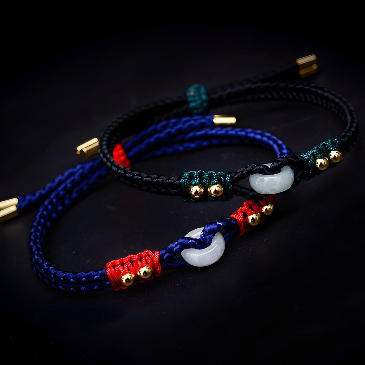 Bracelets en corde tressée noire, rouge et bleue avec pierres de jade blanches et détails dorés.